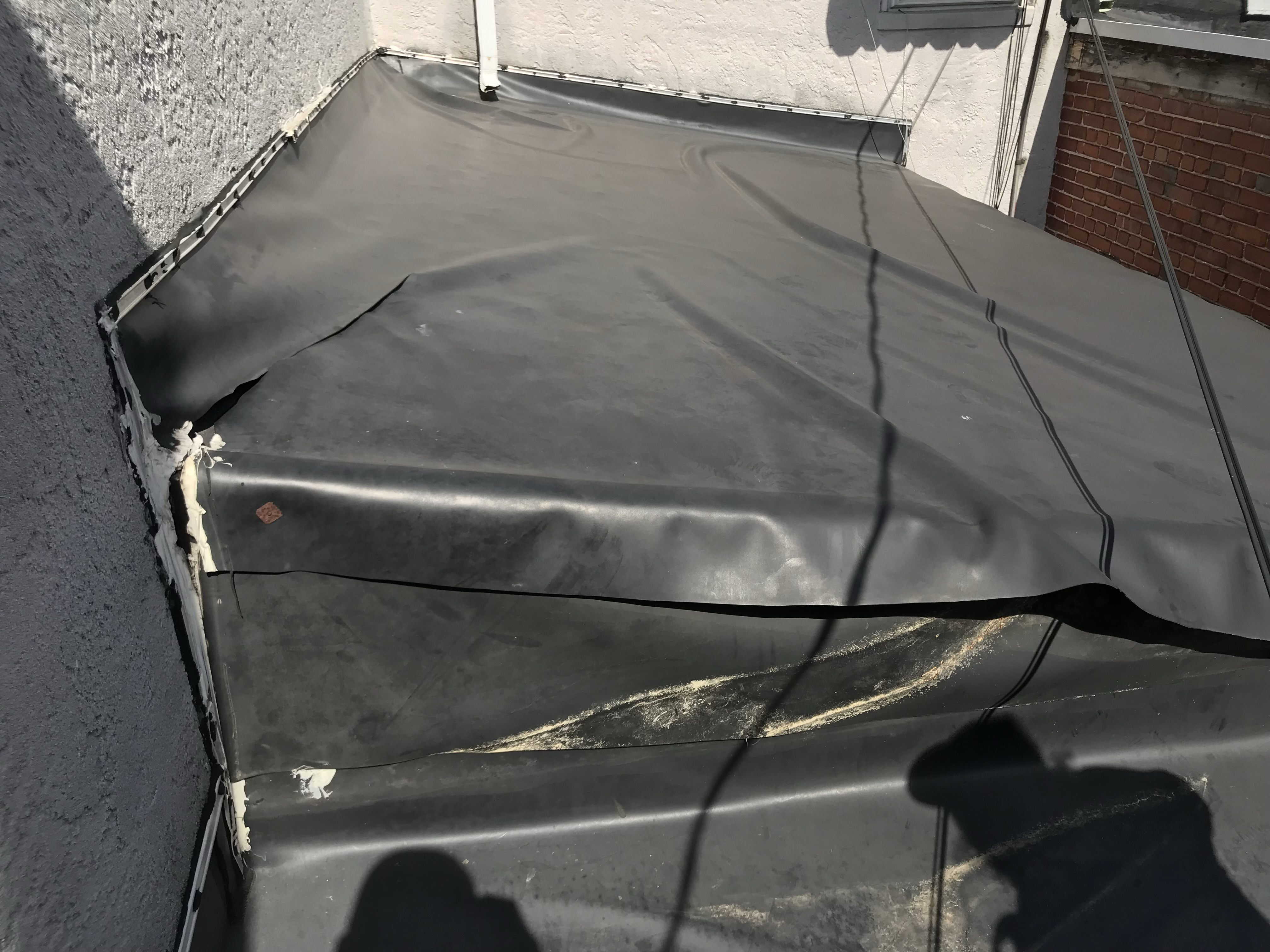 Aged black EPDM flat roof before restoration, leaves and seams visible
