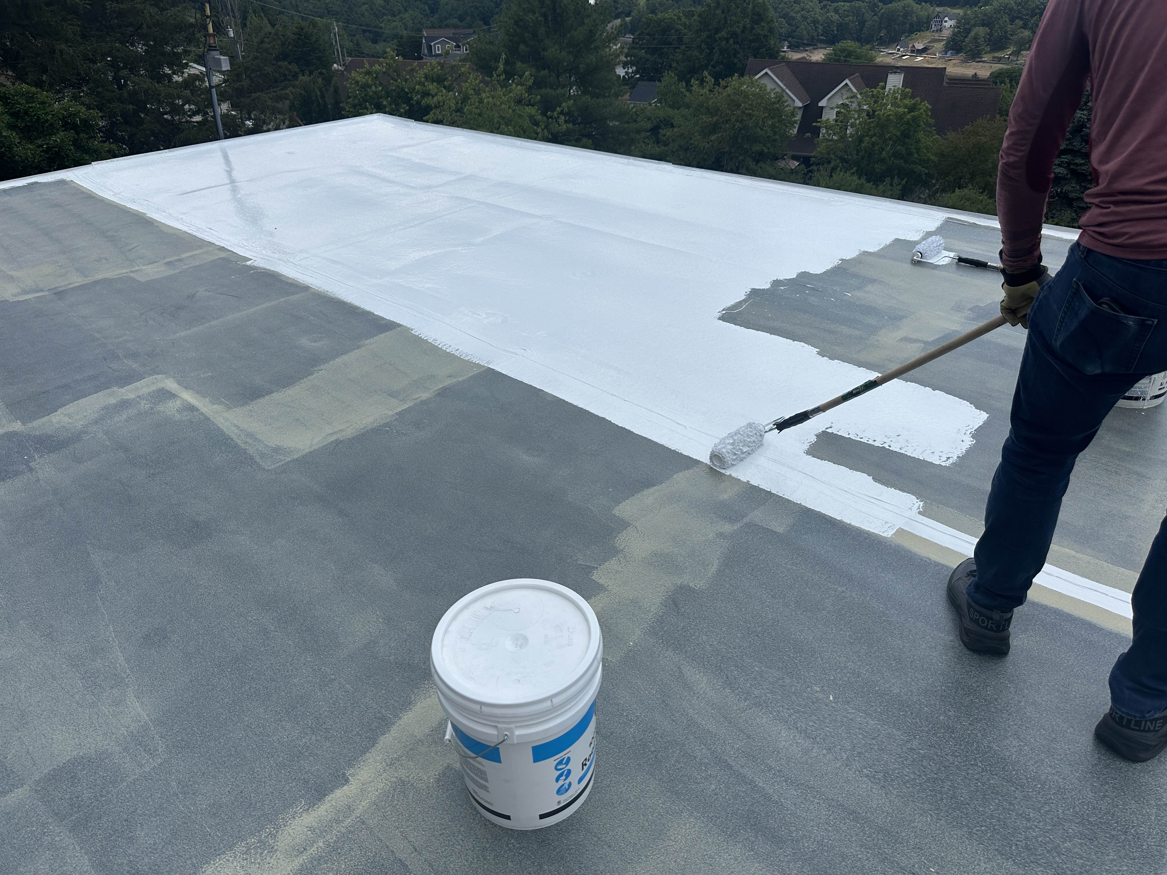 Applying the white silicone topcoat over the primed roof
