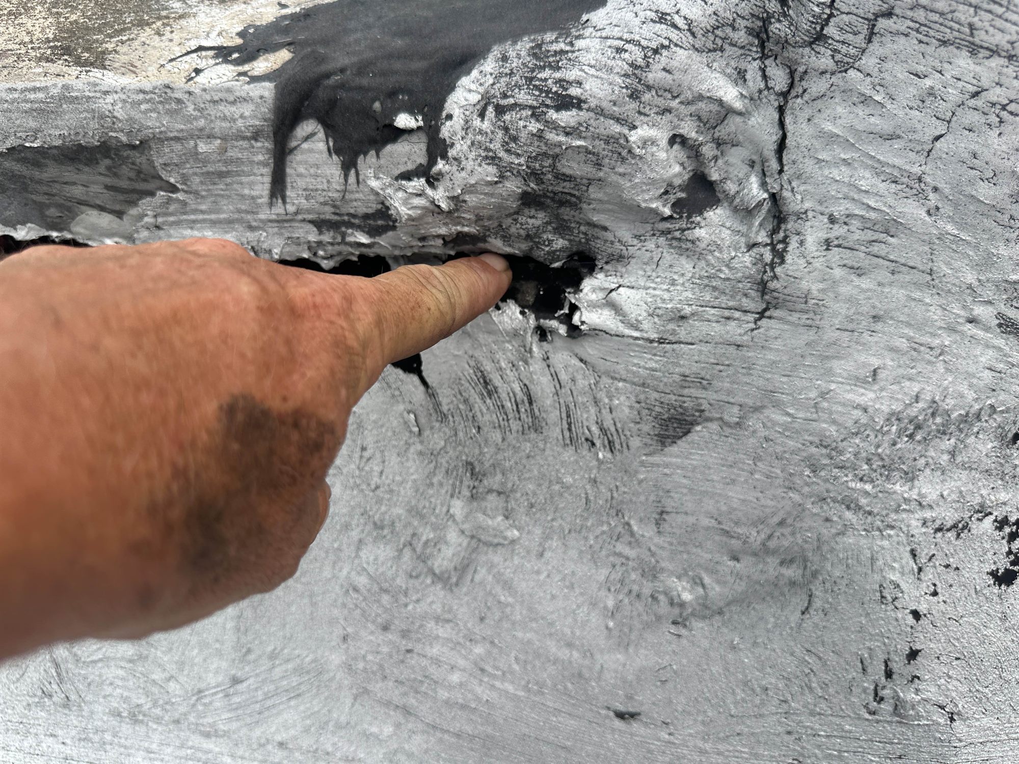 Roofer pointing to a failed void beneath an old roof flashing coating