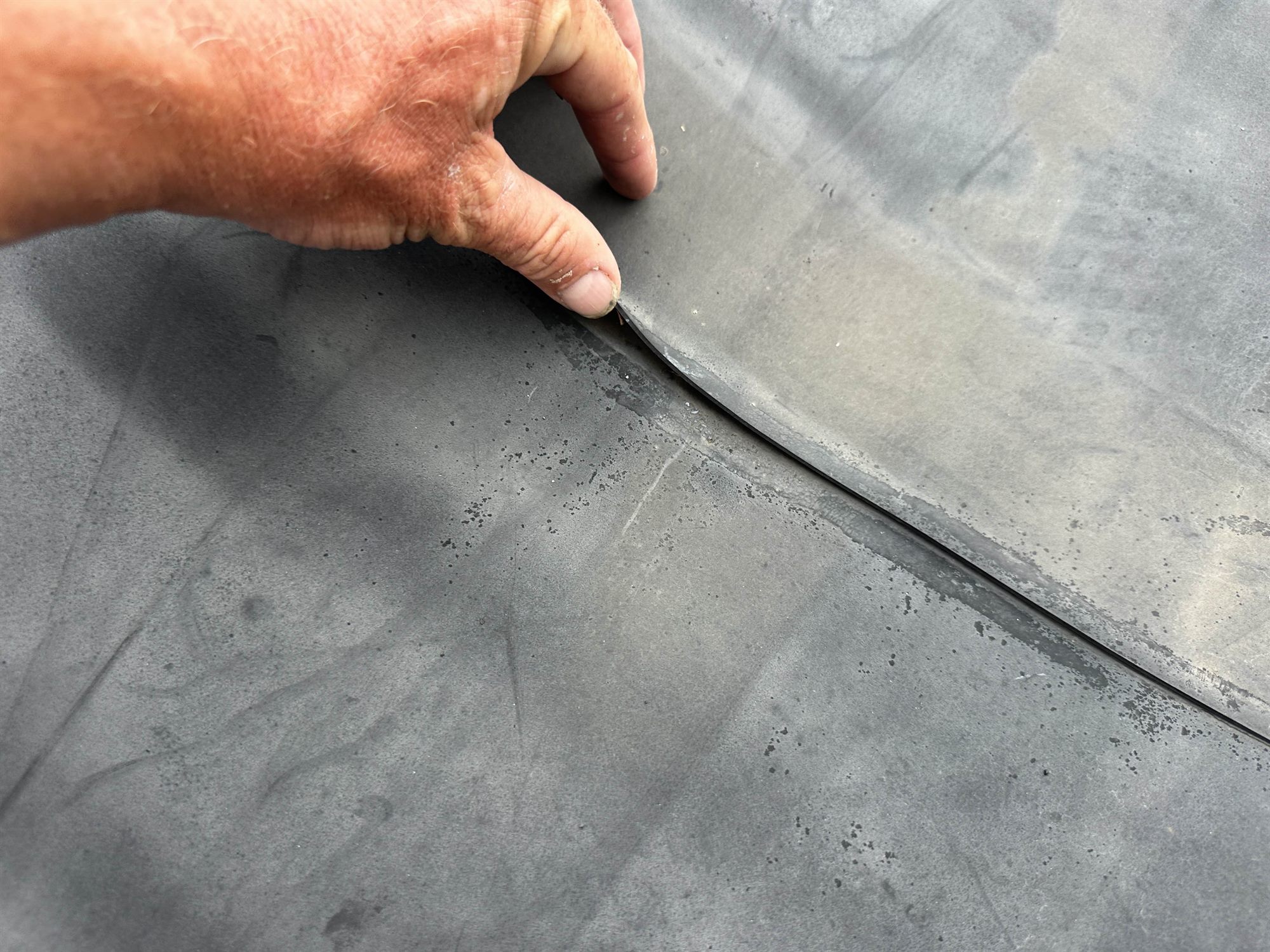 Inspector lifting a failed, unbonded EPDM lap seam by hand during a roof inspection