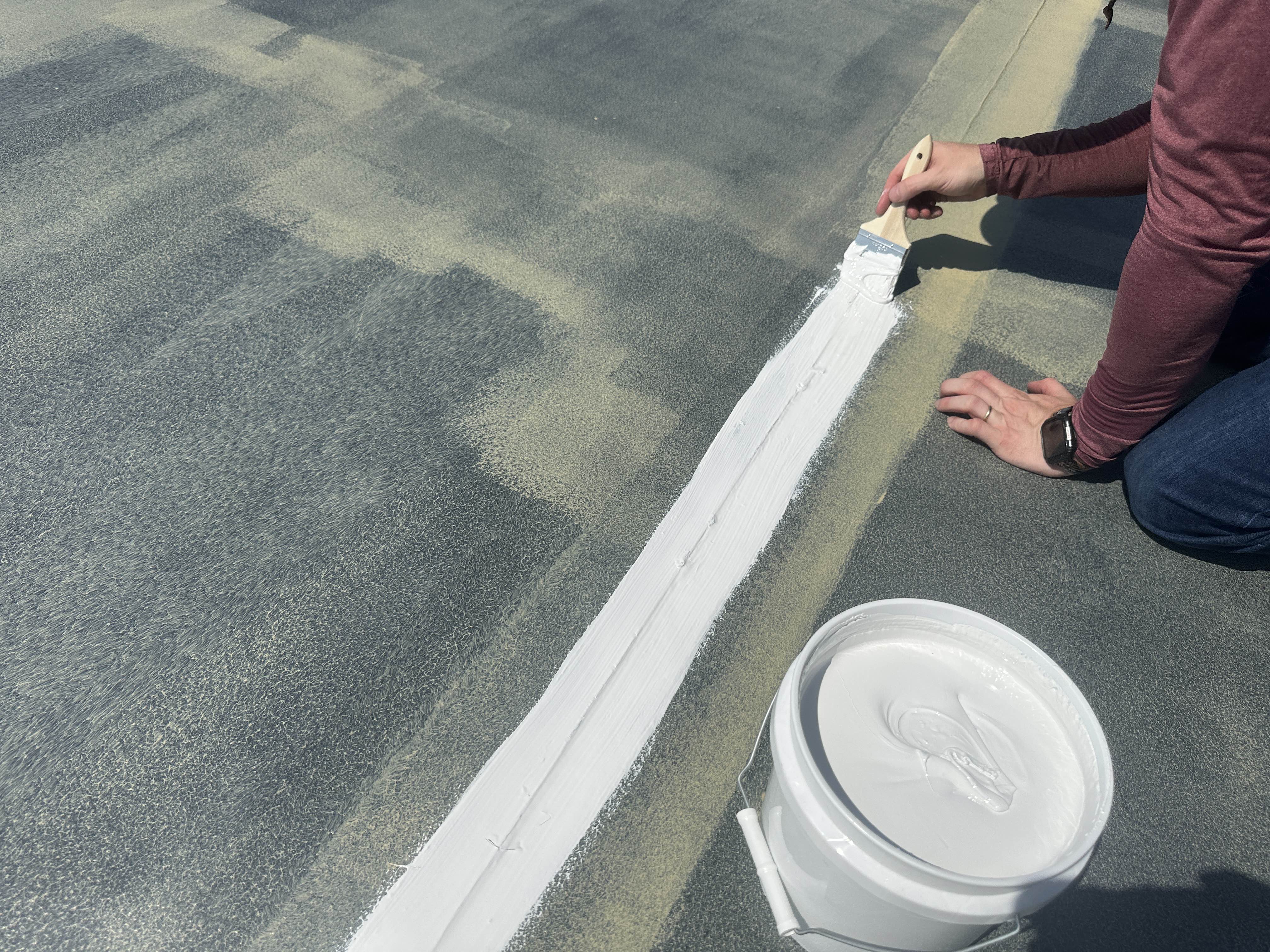 Brushing white flashing compound along a roof seam