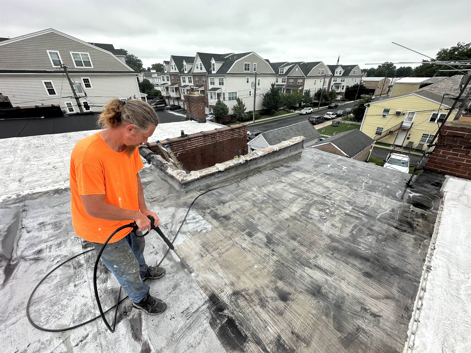 Roofer power washing a flat roof to prep it for silicone coating