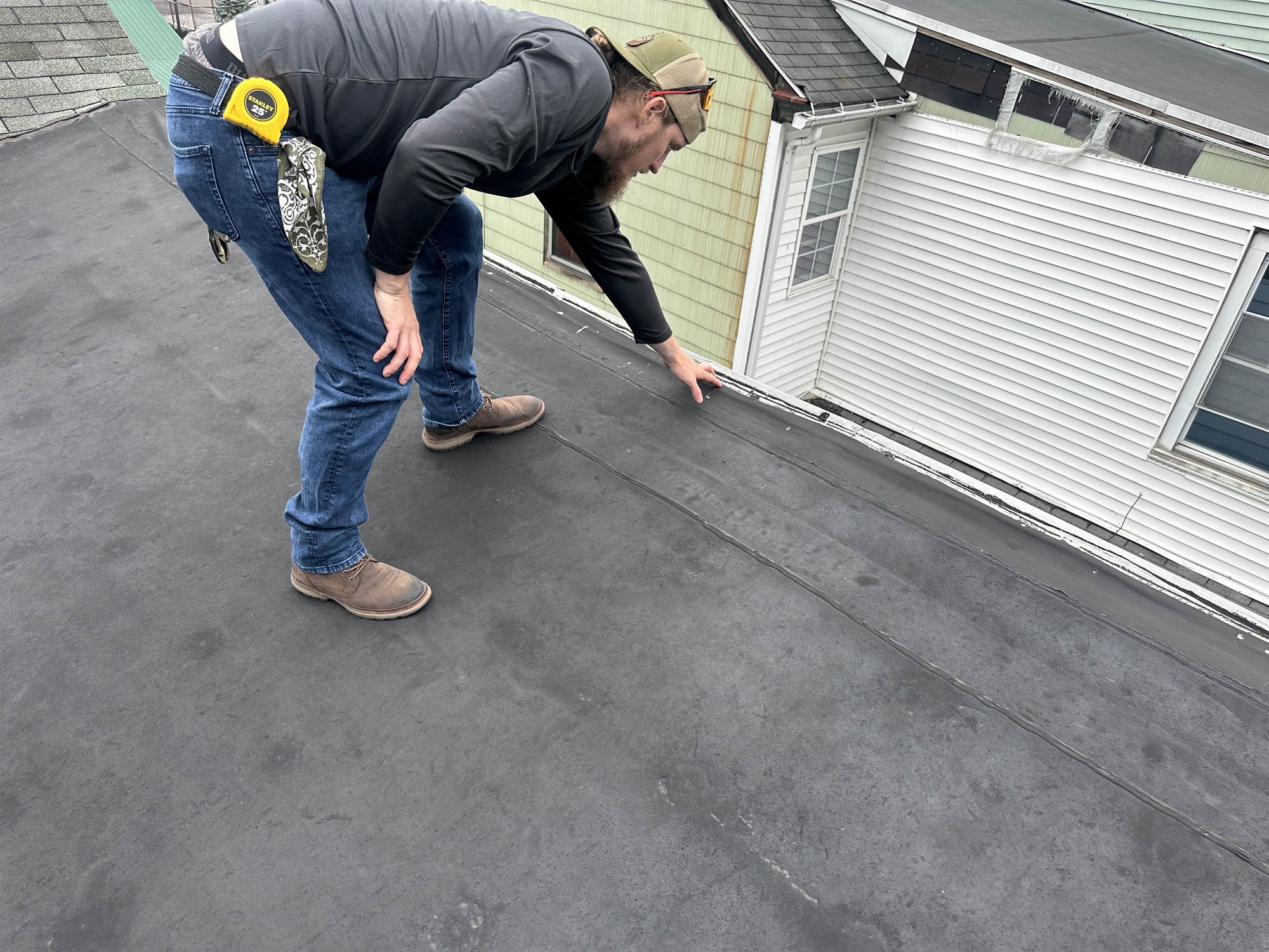 Roofer inspecting the seam and wall edge of a black EPDM flat roof by hand